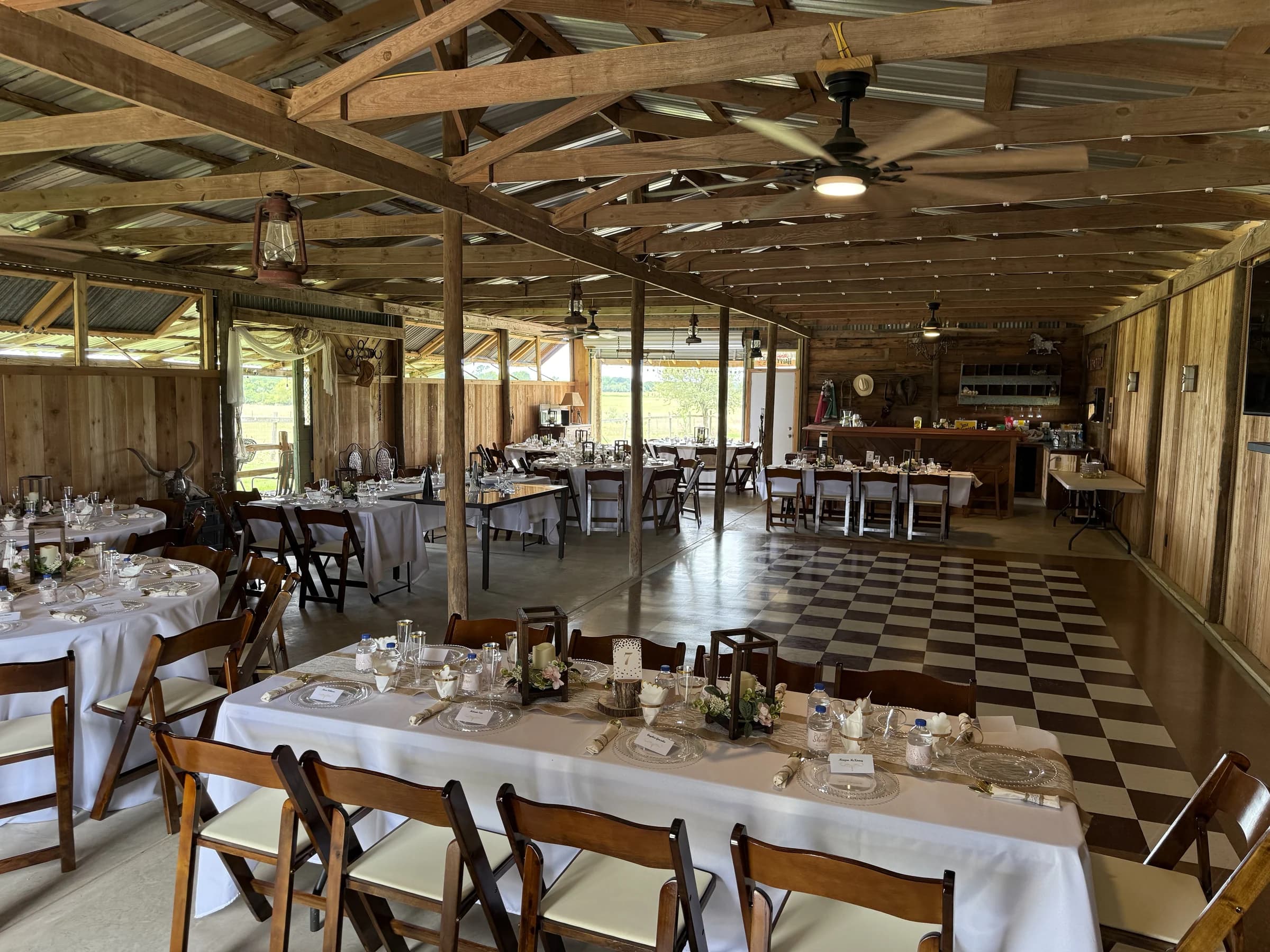 A wide view of the rustic barn with reception tables, exposed rafters, and a checkered dance floor